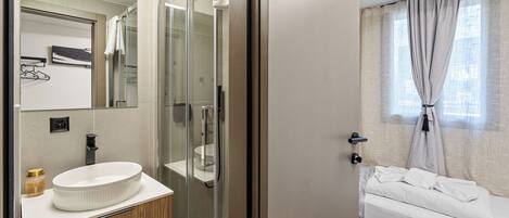 Un baño moderno con cabina de ducha de vidrio, un lavabo blanco y un mueble de tocador de madera.