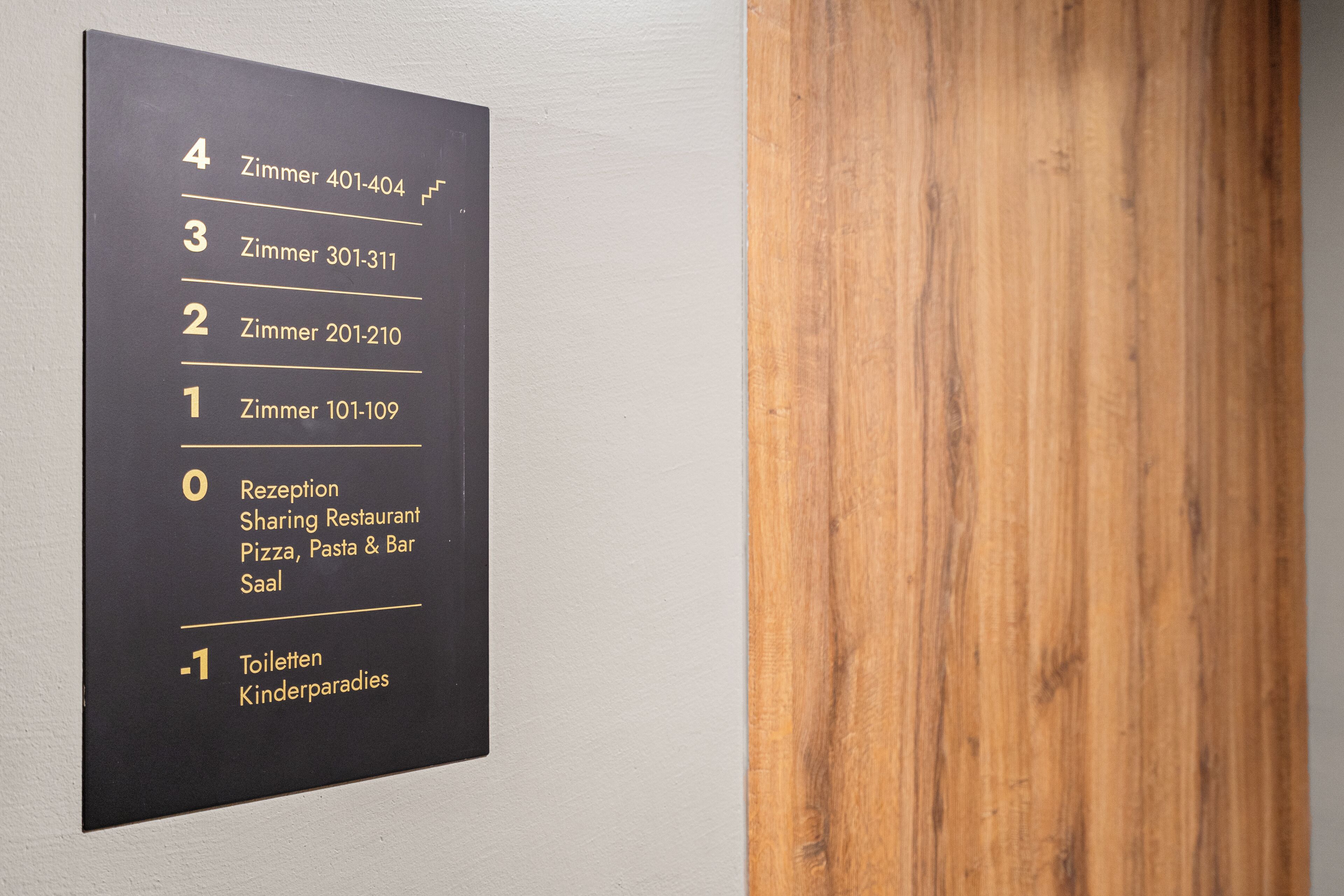 A wall-mounted directory with room numbers and descriptions, including a reception and a children's play area.