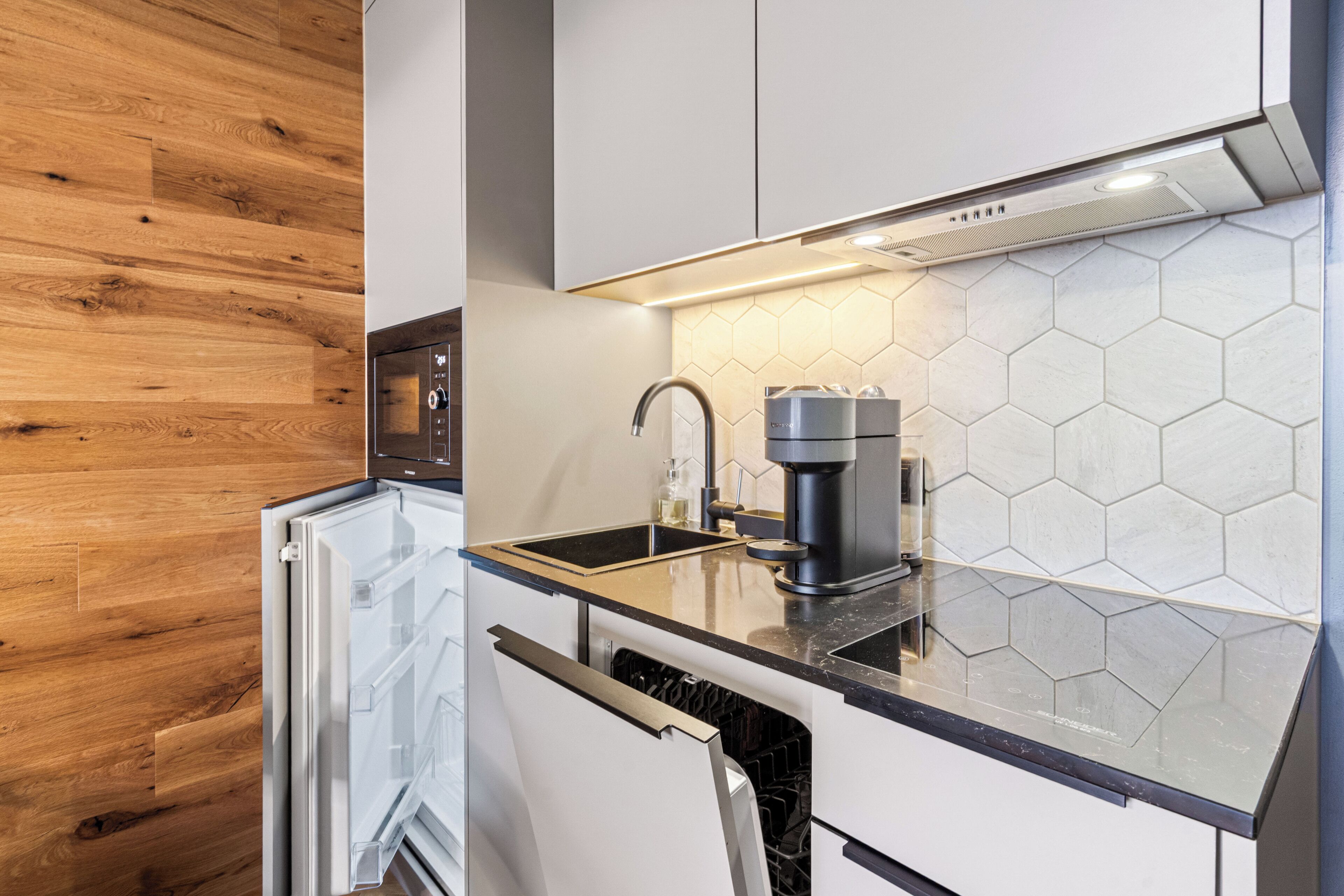 A modern kitchen with a built-in dishwasher, a coffee machine, and a sink with a hexagonal tile backsplash.