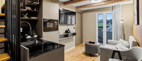 A modern apartment with a kitchen, dining area, and living room. It features a staircase, wooden floors, and a view through a large window.