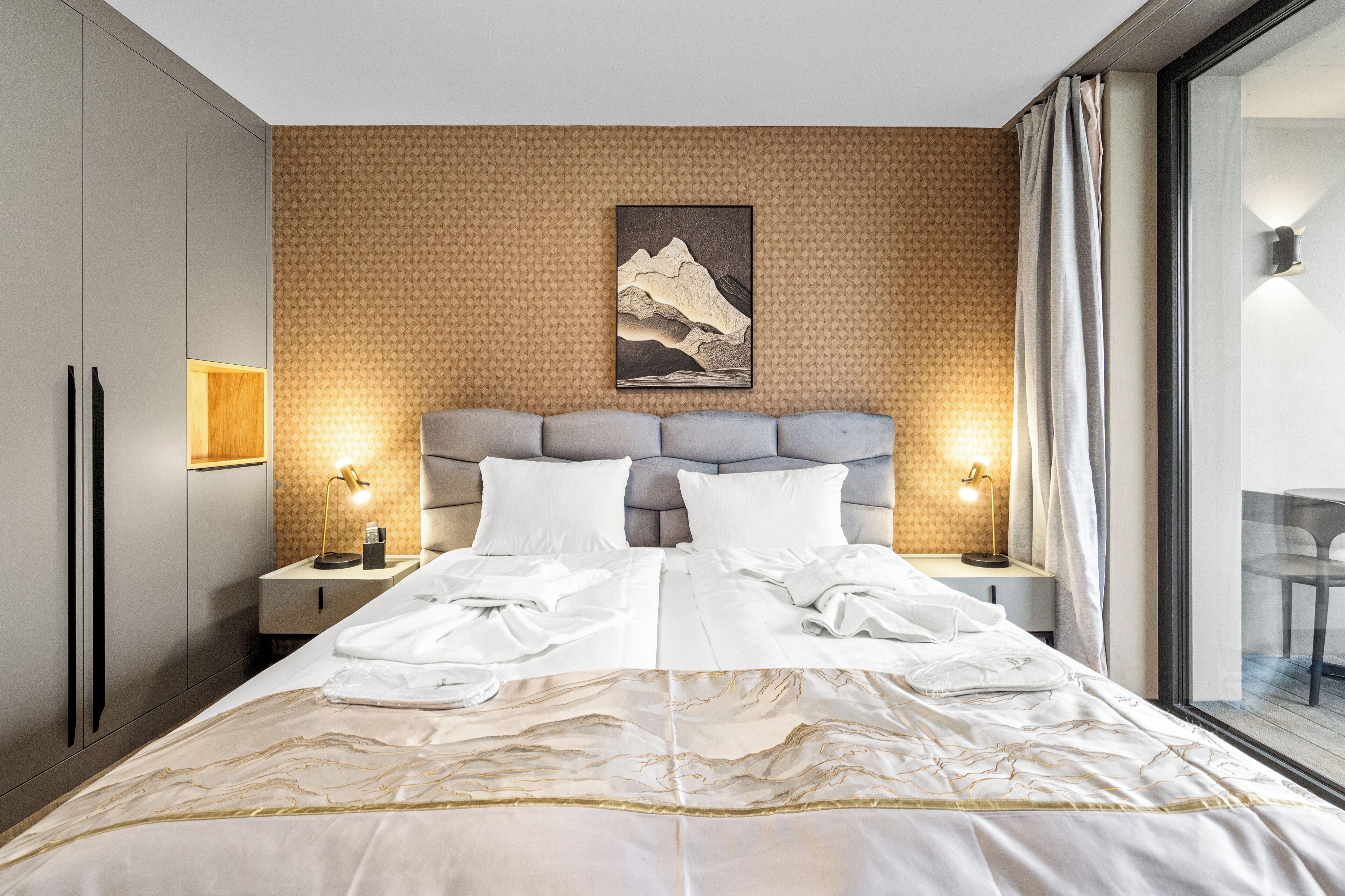 Une chambre d’hôtel moderne avec un grand lit, deux tables de chevet avec des lampes, une tête de lit et une œuvre d’art accrochée au mur.