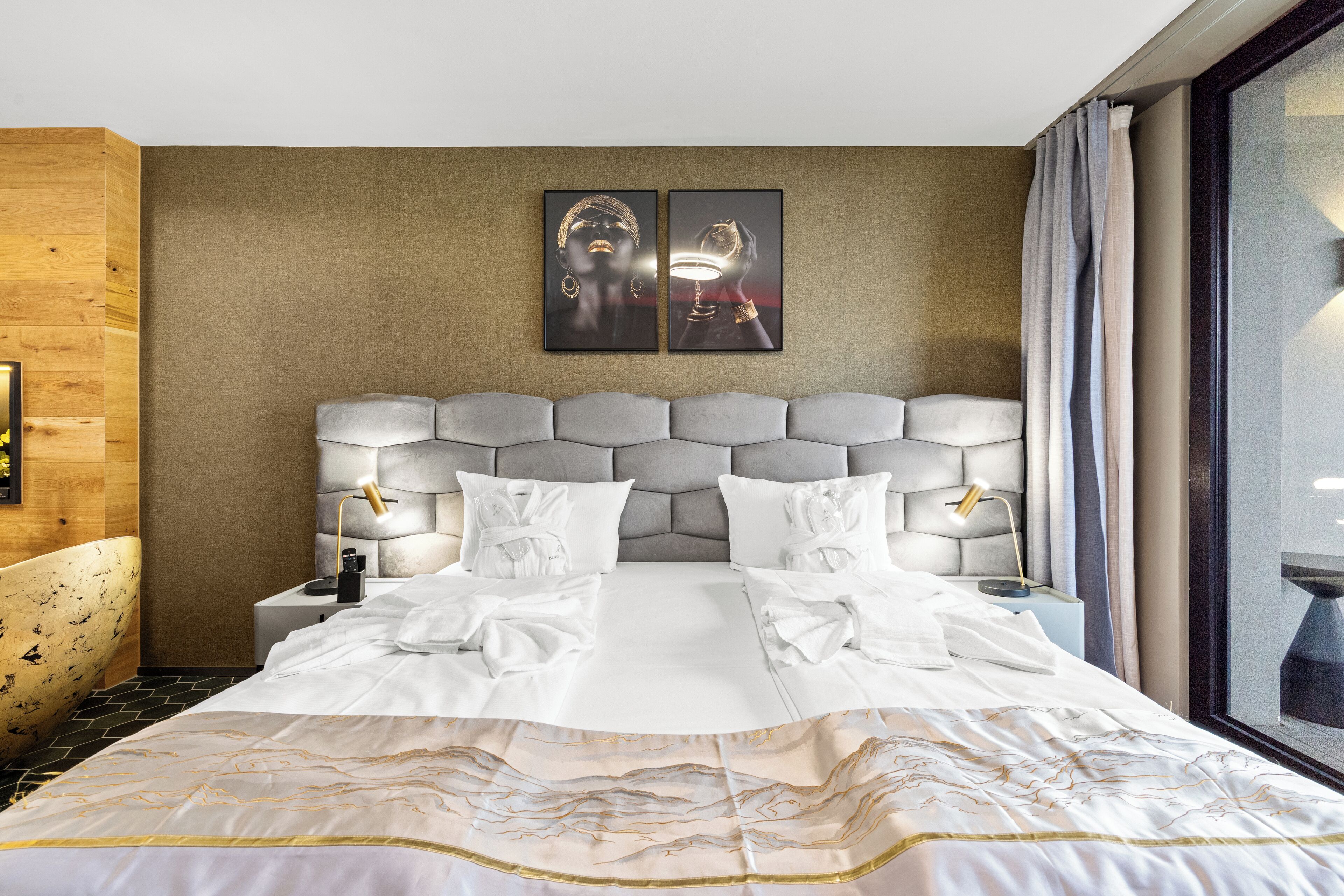 Una habitación de hotel con una cama grande, dos lámparas de noche, un cabecero con diseño acolchado y dos cuadros enmarcados en la pared.