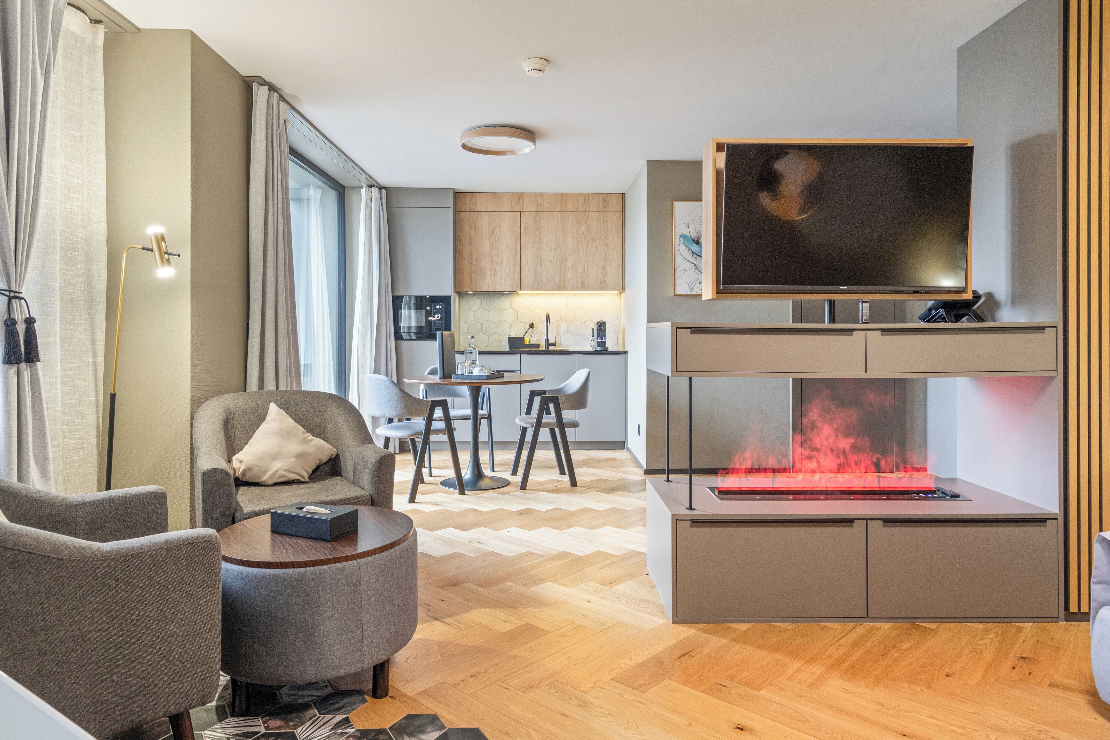 Ein modernes Wohnzimmer mit einem Flachbildfernseher, einem Kamin und einem Essbereich, im Hintergrund befindet sich eine Küche.