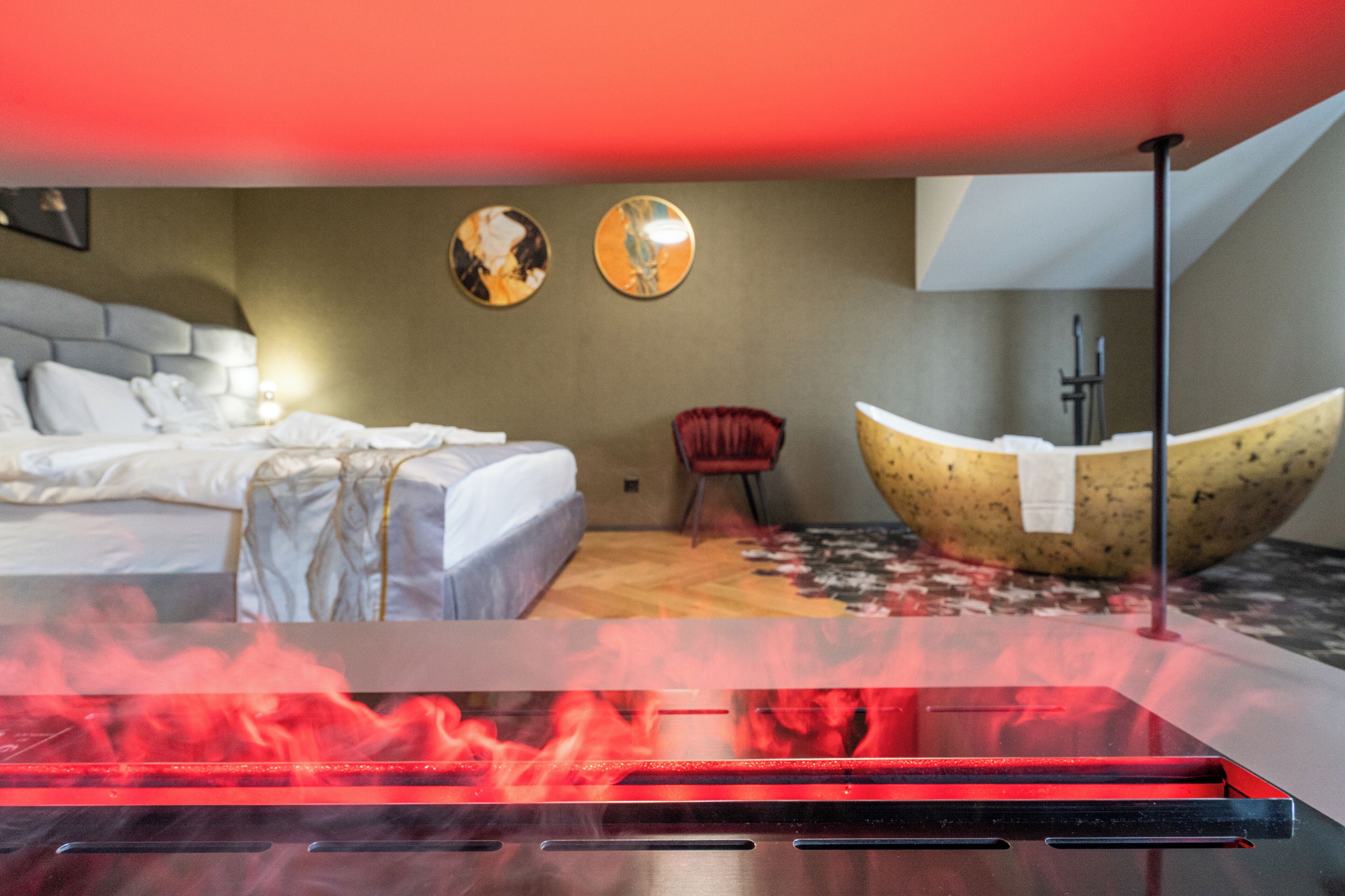 A modern hotel room with a bed, a red chair, a unique spherical light fixture, and a large decorative bowl on the floor.