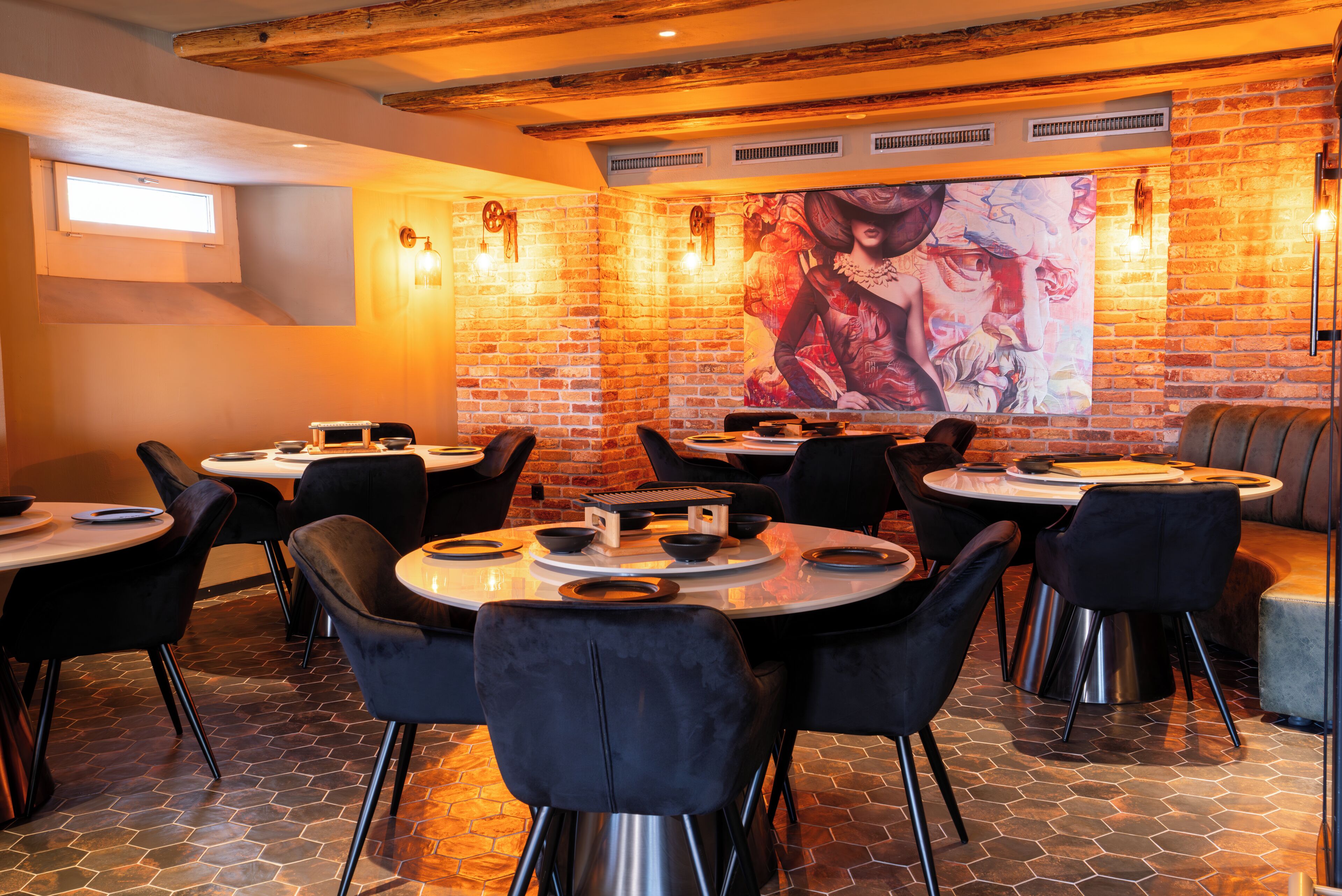 A restaurant with brick walls, black chairs, and round tables.