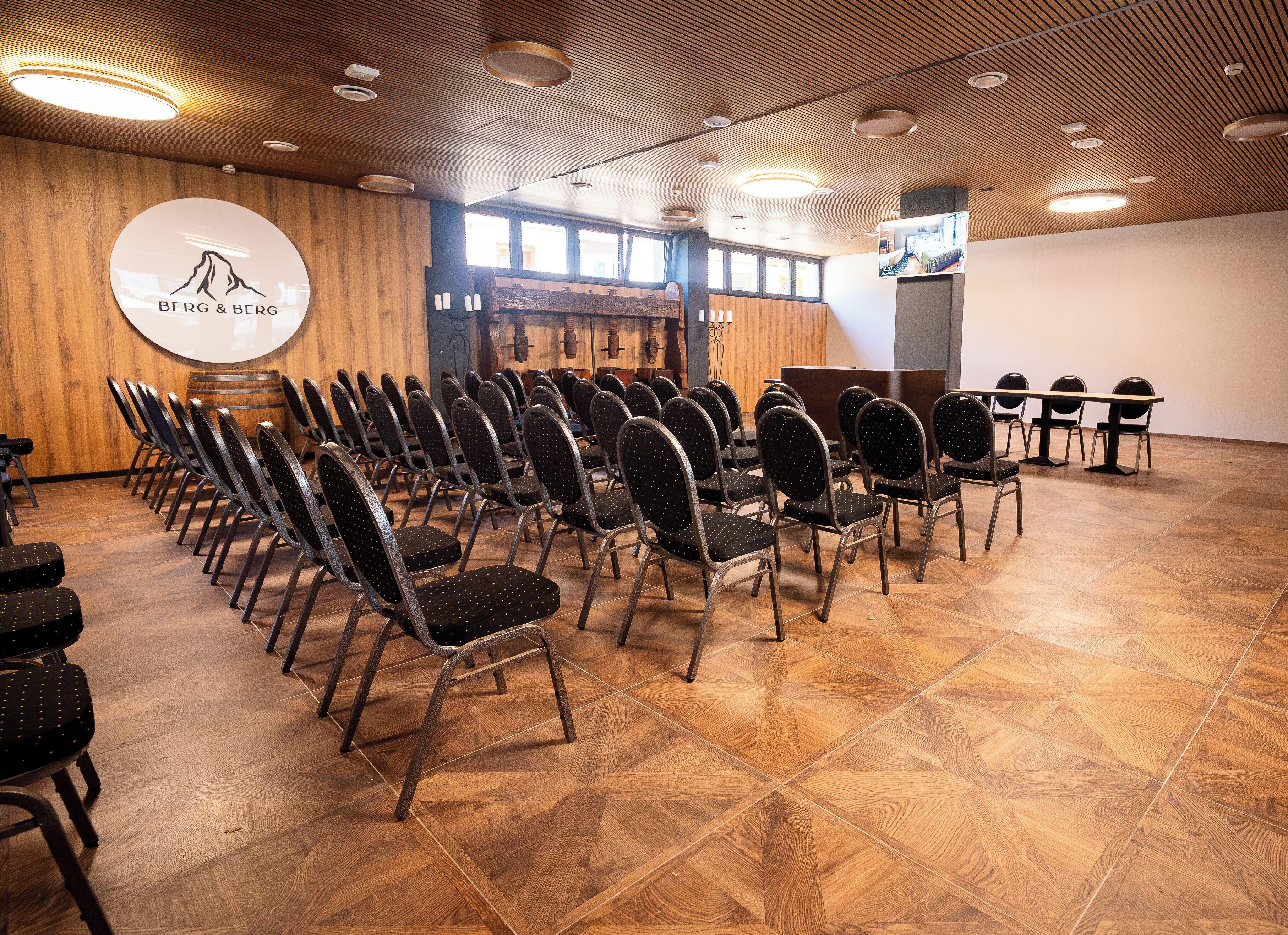 A conference room with rows of chairs, a wooden floor, and a logo on the wall.
