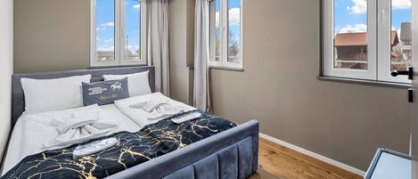 A bedroom with a bed, curtains, a window, and a view of buildings.