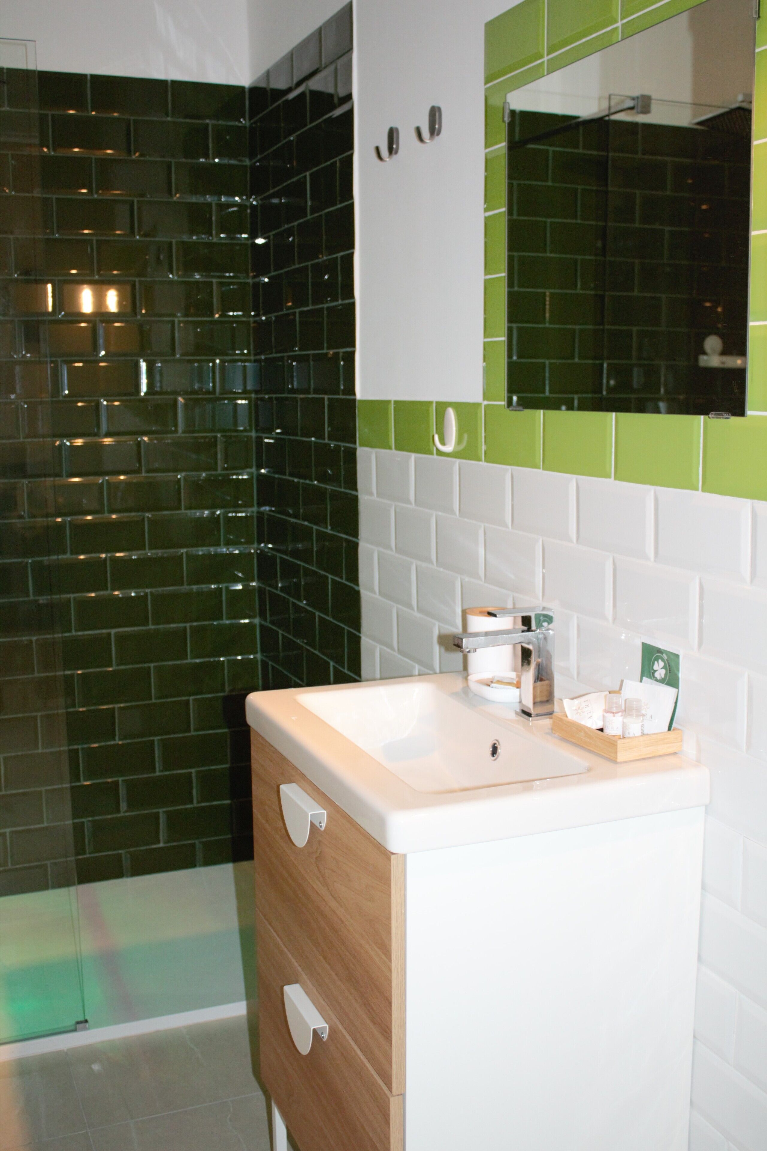 A bathroom with a white sink, wooden cabinet, and green-tiled walls.