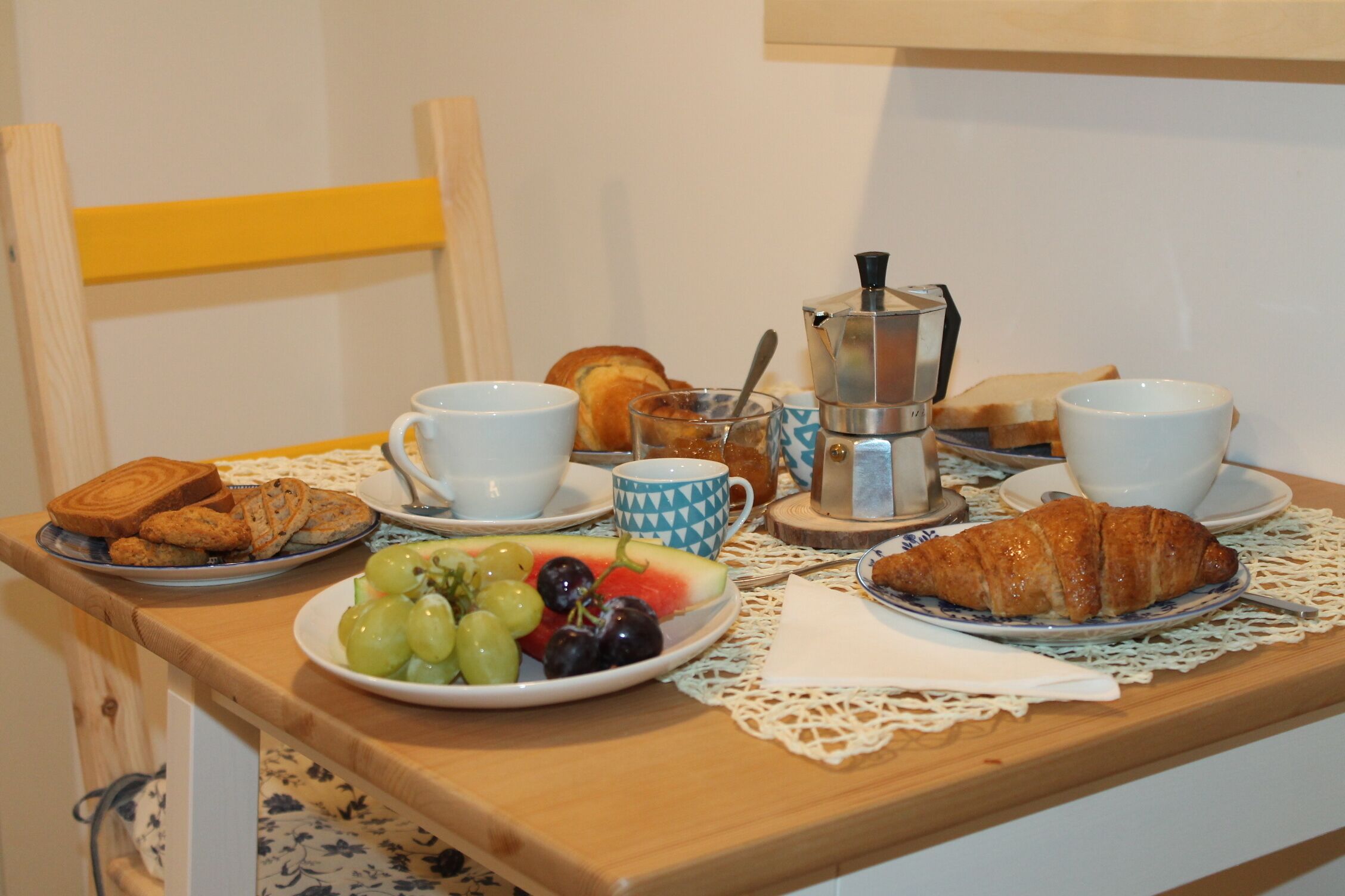 A breakfast table with croissants, bread, fruit, coffee, and cups.