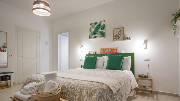 A neatly arranged bedroom with a bed, bedside tables, a wall-mounted shelf, and a hanging plant. - Flegreo bed and breakfast (Naples)