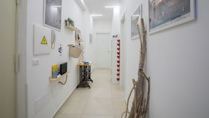 A hallway with white walls, a door at the end, and various items like a phone, a shelf with plants, and a framed picture. - Flegreo bed and breakfast (Naples)