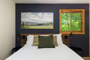 A bedroom with a bed, two bedside lamps, a window with a view of trees, and a landscape painting on the wall. - OTTER'S HOLT - Lakeside retreat with hot tub & sauna (Lombardy)