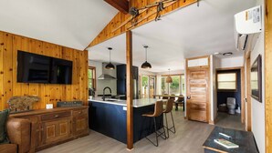 Una cocina moderna con detalles de madera, una isla central, taburetes de bar y un televisor montado en la pared.