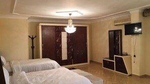 Une chambre avec deux lits, une armoire, une télévision et un lustre.