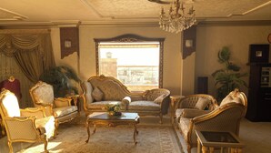 Un salon luxueux, agrémenté de meubles richement décorés, d’un lustre et d’une grande fenêtre offrant une vue imprenable.