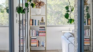 Un interior moderno con una estantería, plantas colgantes y una ventana con vistas a árboles.