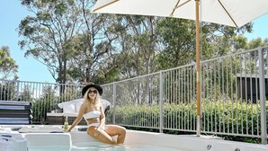 Una persona sentada en un jacuzzi con una sombrilla blanca y una cerca blanca al fondo.