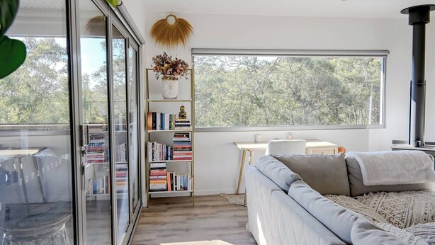 Una sala de estar moderna con un ventanal grande, una estantería, un sofá y un ventilador de techo.