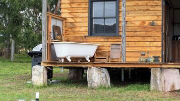 A rustic cabin with a porch, a bathtub, and a small deck area.