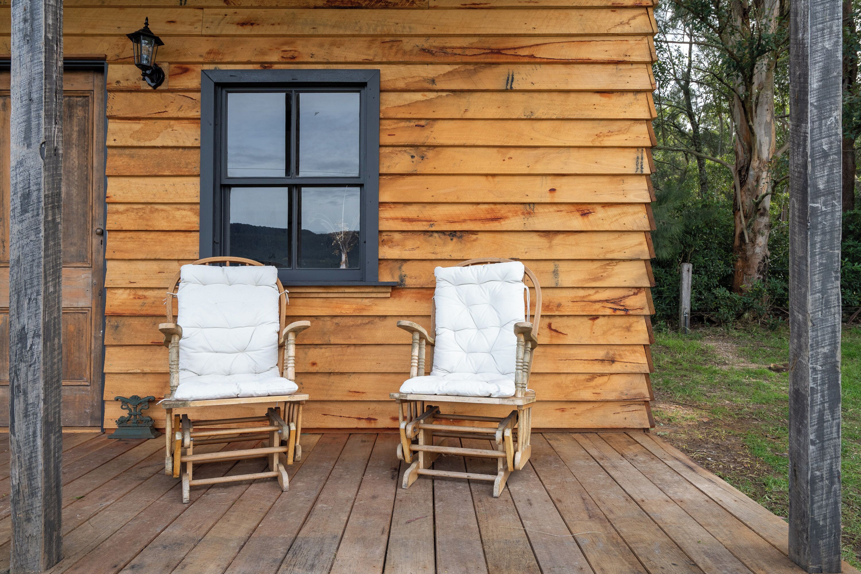 Two wicker rocking chairs on a wooden deck in front of a wooden cabin with a window.