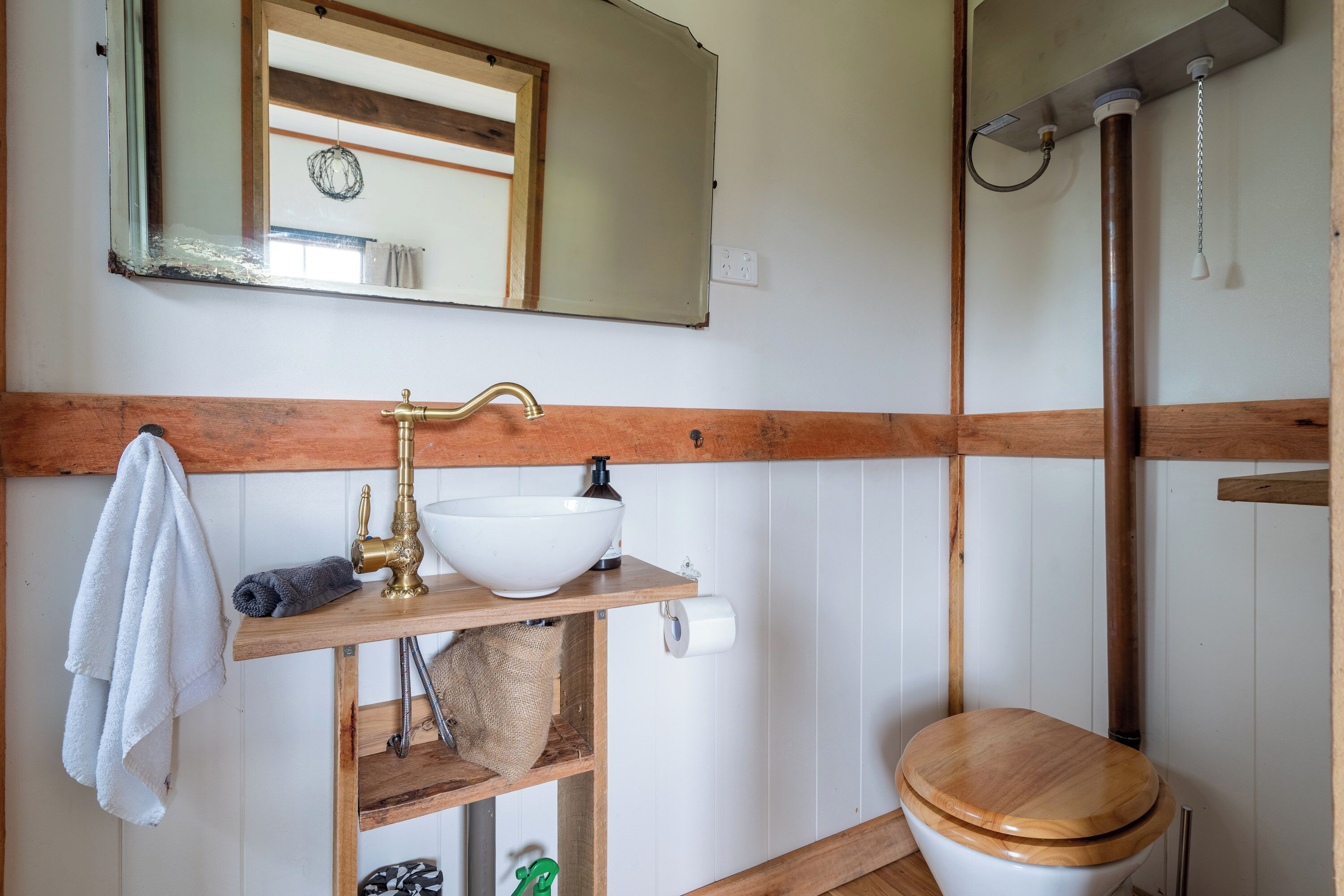 A bathroom with a wooden vanity, a white sink, a toilet, and a mirror.
