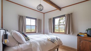 Un dormitorio con cama, dos ventanas, una mesita de noche con vela y un aparador de madera.