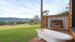 Un baño con una bañera independiente, una terraza de madera y una vista panorámica de un campo con colinas.