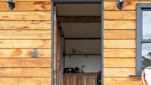 Una cabaña de madera con un porche, un área de cocina visible a través de una puerta abierta y dos faroles fijados a la pared.