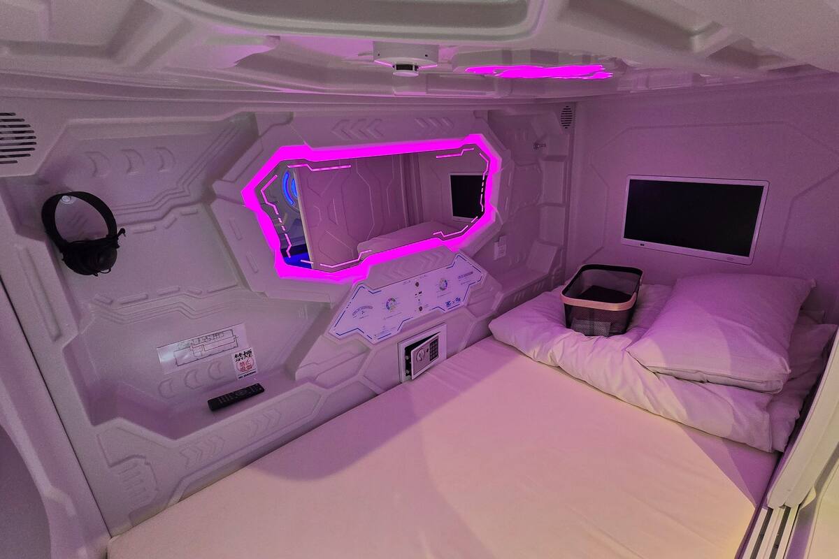 Ein Zimmer mit einem Bett, einem kleinen Tisch, einem an der Wand montierten Fernseher und einer Bedienkonsole mit Knöpfen und Drehreglern.