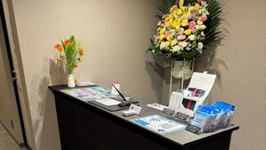 A reception desk with informational brochures, a name tag, and a floral arrangement. - HOTEL GALAXY POD (Koshigaya)