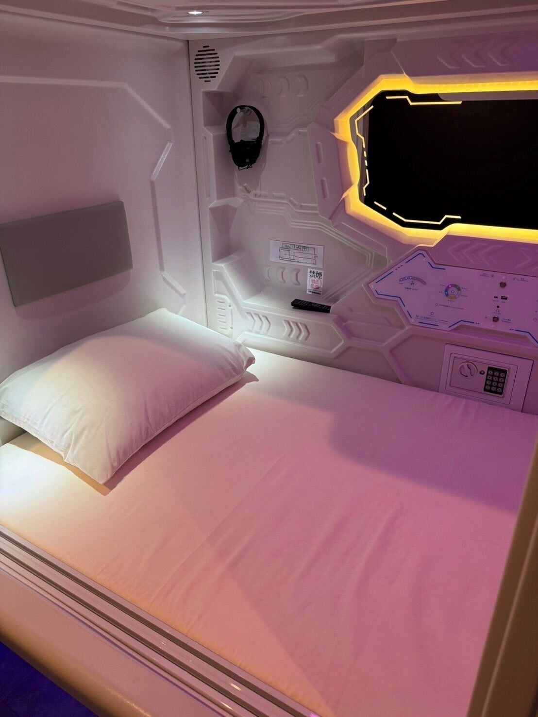 A modern, compact room with a bed, a control panel, and a headboard.