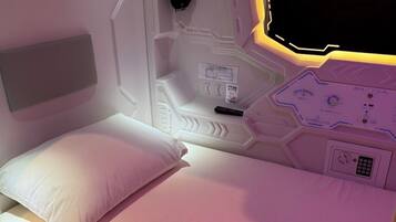 A modern, compact room with a bed, a control panel, and a headboard.