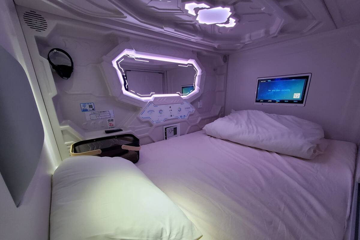 Ein modernes Hotelzimmer mit einem ordentlich bezogenen Bett, einer Bedienkonsole und einem digitalen Bildschirm, der eine Meldung anzeigt.