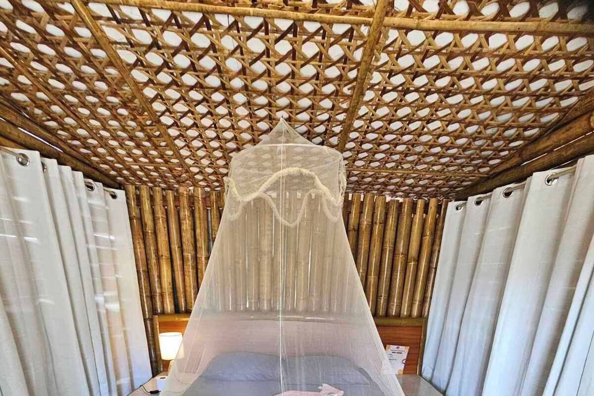 A room with a bed covered by a mosquito net, bamboo flooring, and a wooden ceiling structure.