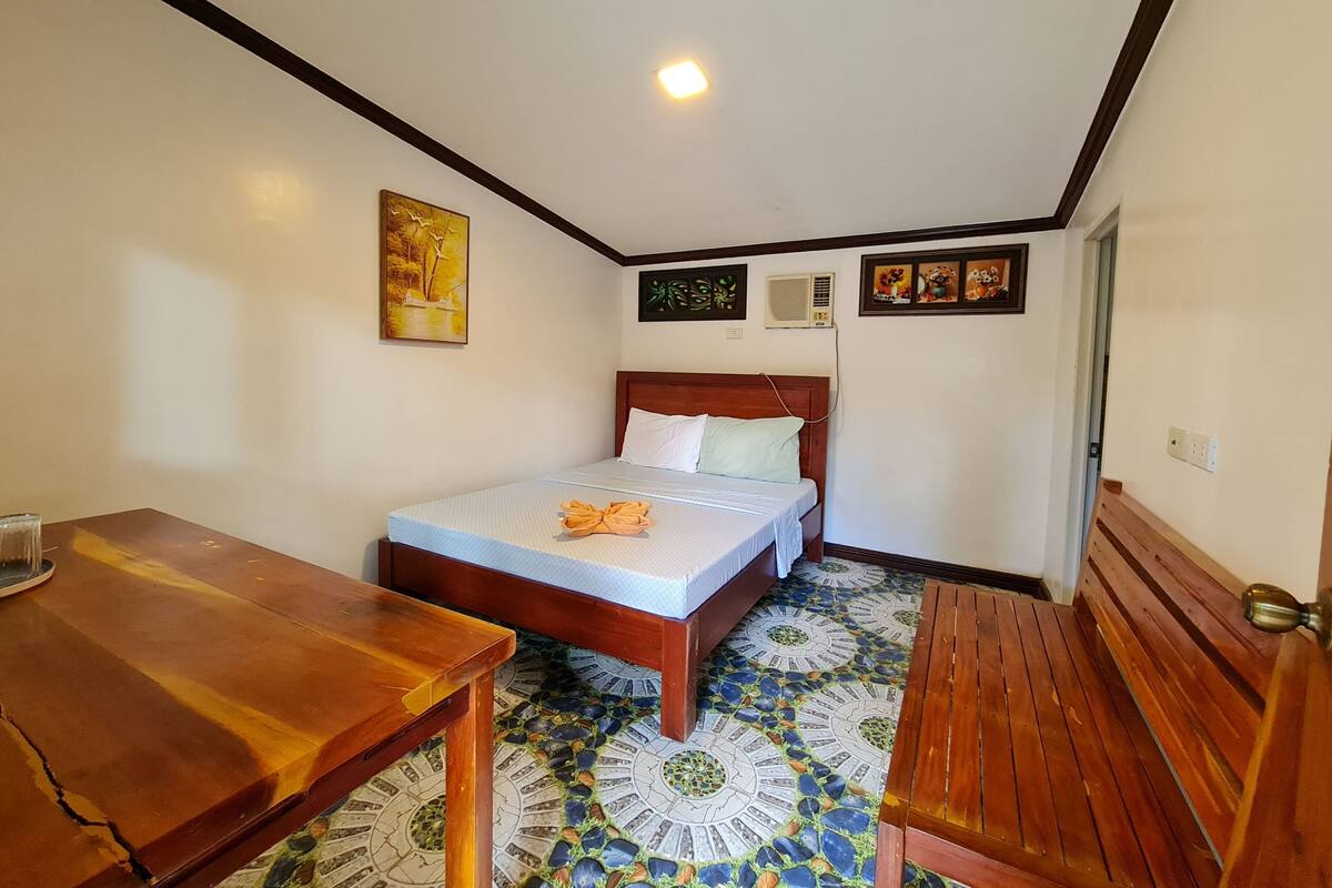 A small, cozy room with a bed, a wooden table, and a bench.