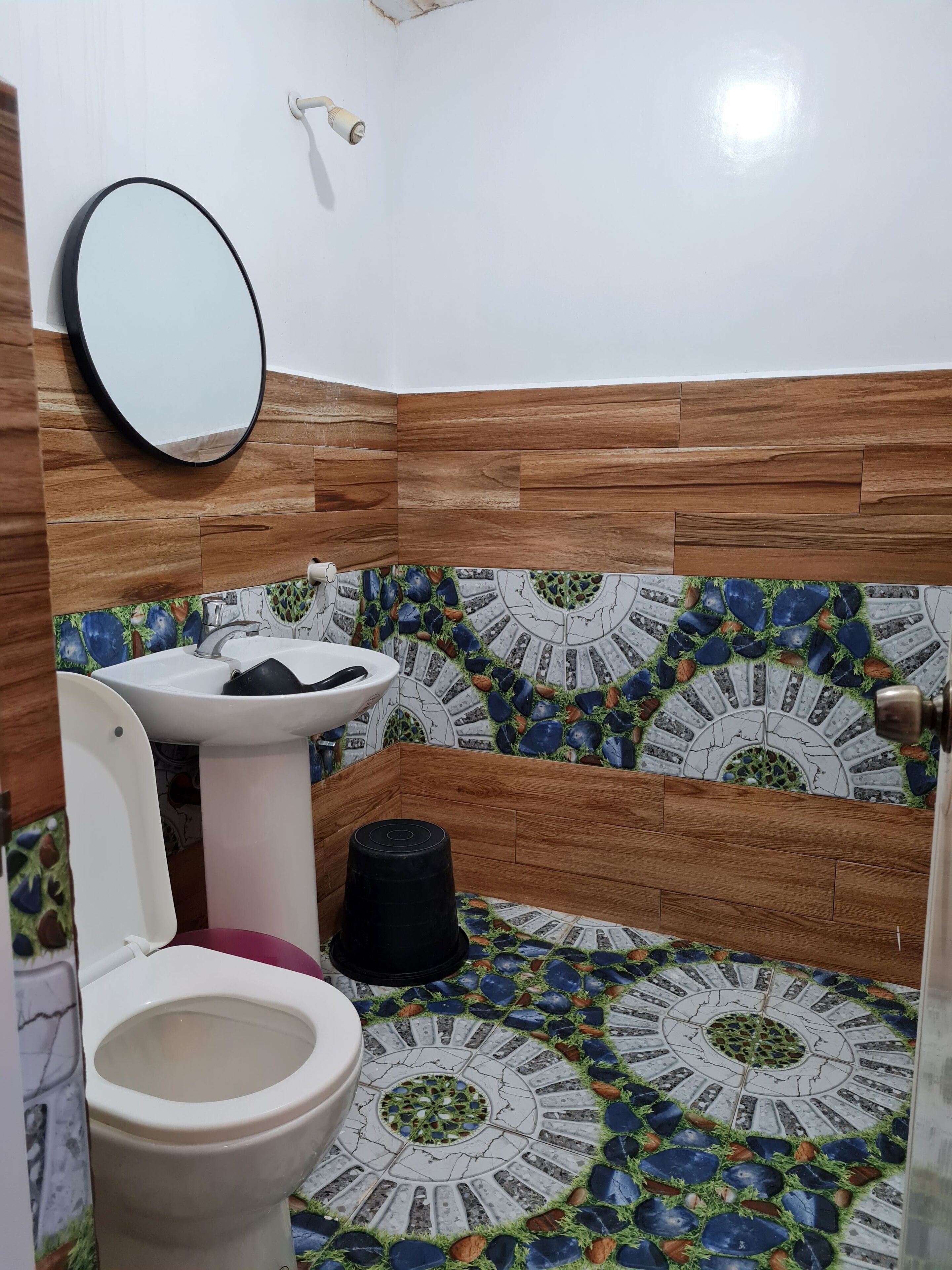 Un baño con un panel de pared de madera, un lavamanos blanco, un inodoro y un suelo decorado con baldosas.