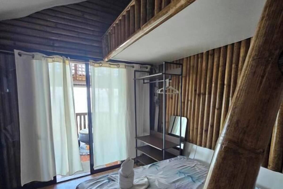 A bedroom with a bunk bed, a bed with a patterned bedspread, a bedside table, and a window with curtains.
