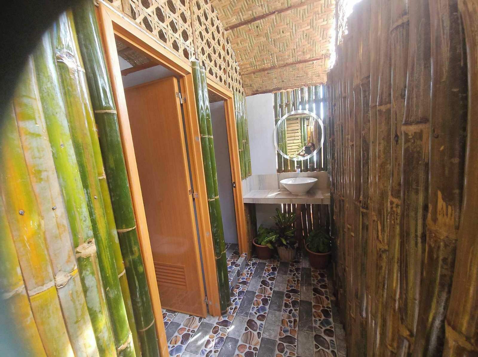 Une salle de bain avec une porte en bambou, un miroir, un lavabo et des plantes en pot.