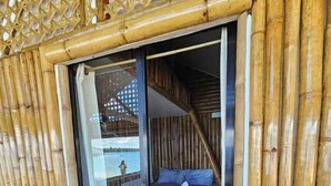 A bamboo-framed room with a bed, a sliding glass door, and a view of a lake. - Tambayan Rooms & Cottages by SMS Hospitality (Loay)