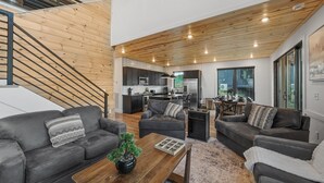 Ein modernes Interieur mit Treppe, grauen Sofas, einem Holztisch und einer Küche im Hintergrund.