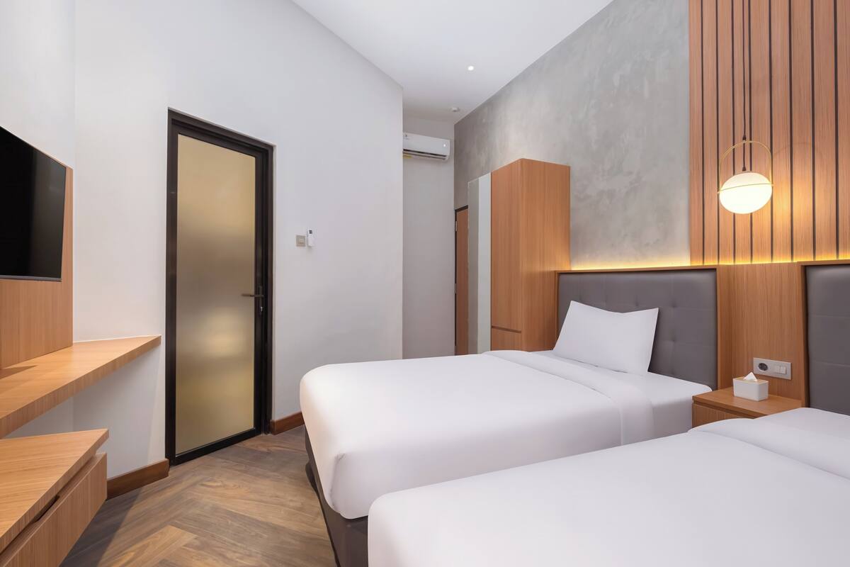 Een hotelkamer met twee bedden, houten hoofdeinden, een ingebouwde televisie en een wandlamp.