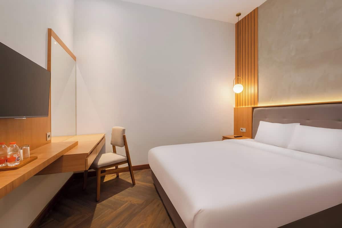 Een hotelkamer met een bed, een bureau, een stoel, een televisie en een wandlamp.
