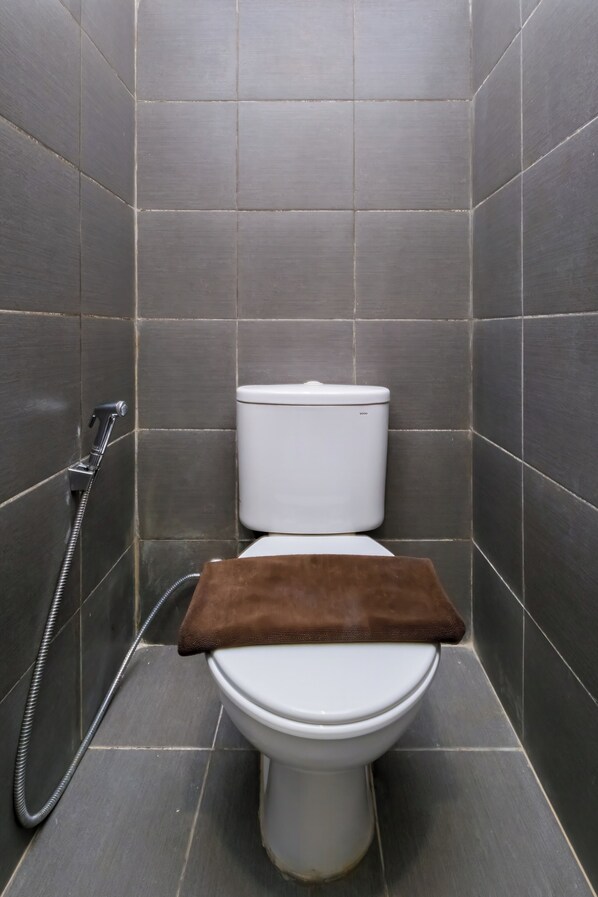 A small, modern bathroom with a white toilet, a shower head, and a brown towel on the seat.