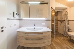 A modern bathroom with a white sink, wooden vanity, a large mirror, and a shower area. - Seeschwalbe 330 - The Scandinavian family home for 4 with sauna and whirlpool (Mirow)