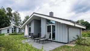 Una casa moderna con un patio cubierto, mobiliario exterior y un ventanal grande.