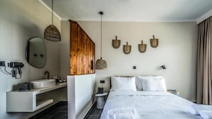 A modern hotel room with a large bed, a built-in vanity, a hanging light fixture, and wall-mounted artwork. - Elion Seaside by Anayia All Inclusive Resorts (Chalcis)