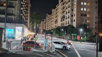 Una calle urbana nocturna con edificios residenciales de varios pisos, una farmacia y un paso de peatones.