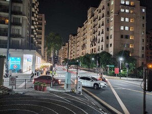 A nighttime urban street with multi-story residential buildings, a pharmacy, and a pedestrian crossing. - 1 Bed Apartment - Sleeps 7 - Pool & Wifi (Pasay)