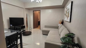 A modern living room with a flat-screen TV, a glass-top dining table, a beige sofa, and a large potted plant. - 1 Bed Apartment - Sleeps 7 - Pool & Wifi (Pasay)
