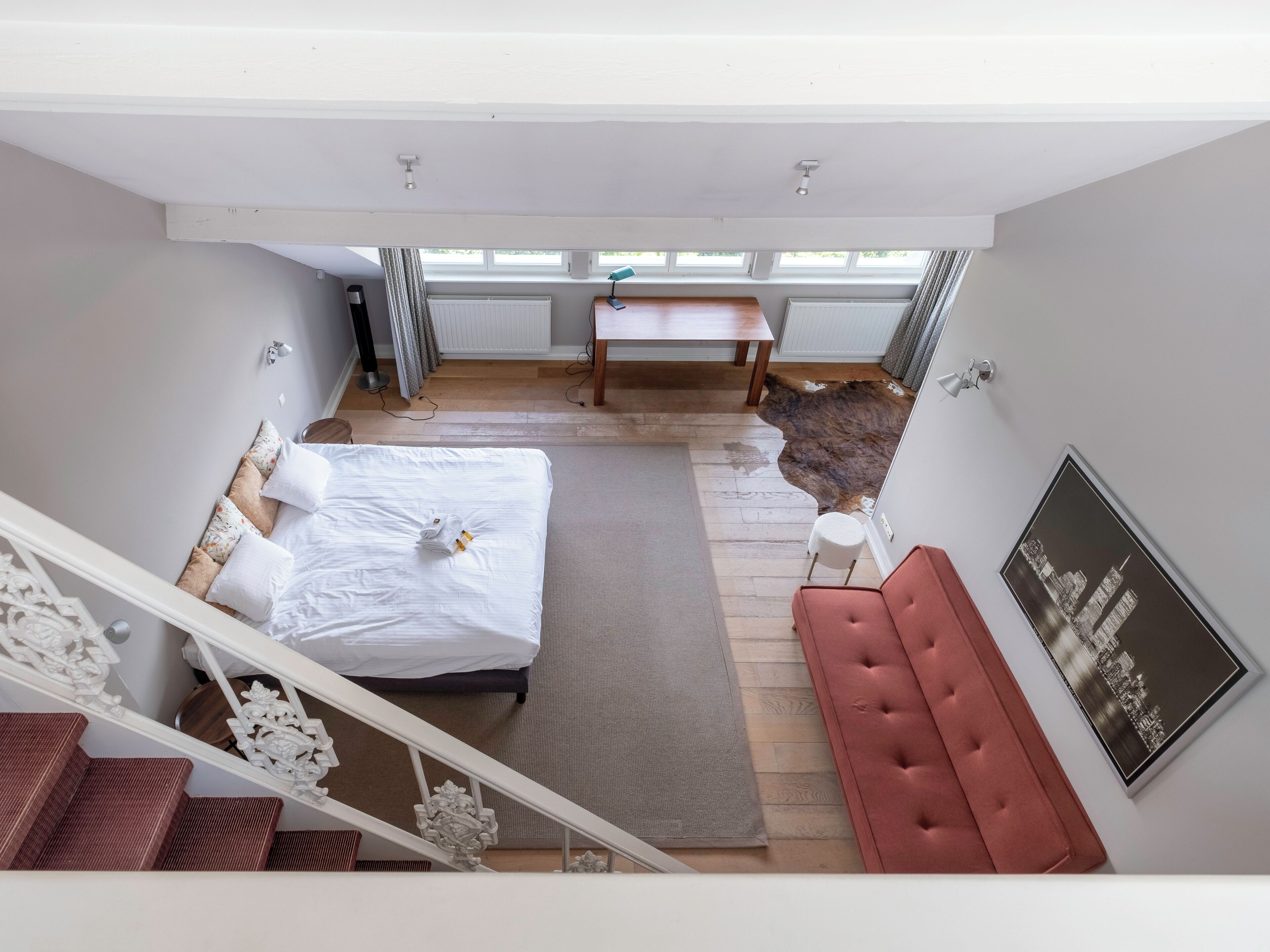 Un dormitorio amplio con una cama grande, un sofá rojo, una mesa de comedor y una obra de arte con temática urbana en la pared.